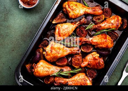 Gebackene Hähnchenbeine, Drumsticks mit süßen Feigen und Zwiebeln in balsamischer Marinade auf schwarzem Backblech, rostiger grüner Tischhintergrund, Draufsicht Stockfoto