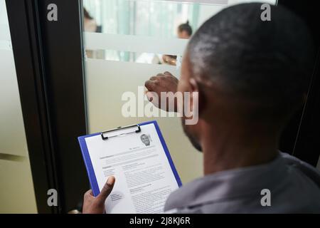 Bewerber mit gedrucktem lebenslauf in den Händen klopft an die Tür der Personalabteilung des Unternehmens Stockfoto