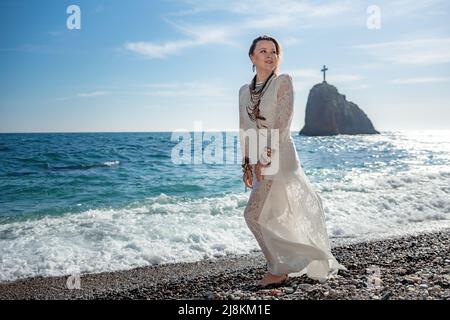 Frau in böhmischer Kleidung am Strand bei Sonnenuntergang. Boho-Stil für modischen Look im Resort. Frau mittleren Alters gut aussehende Frau in weißem Kleid und Boho-Stil Stockfoto