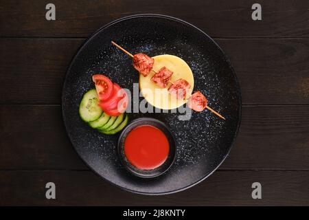 Gebratene Wurst auf Spieß mit Kartoffelpüree und Scheiben frischer Tomaten und Gurken Stockfoto