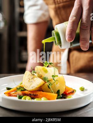 Küchenchef gießt gesundes Gourmet-Gericht mit grüner Sauce Stockfoto