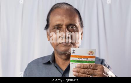 Birbhum, Westbengalen / Indien - 15. März 2022: Selektiver Fokus auf die Aadhaar-Karte, die von einem alten indischen Mann mit lächelndem Gesicht in der Hand gehalten wird Stockfoto