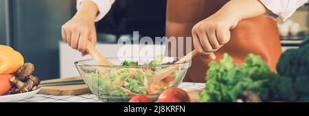 Asiatische Frau mischt die Zutaten in einer Salatschüssel am Küchentisch. Stockfoto