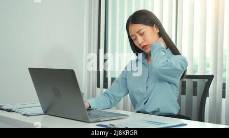 Junge asiatische Frau sitzt bei der Arbeit und hat Schmerzen im Nacken, während sie im Büro sitzt und arbeitet. Stockfoto