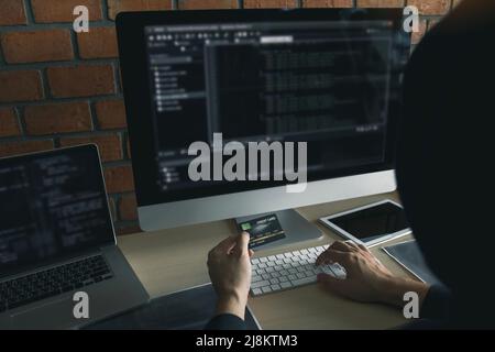 Hacker in der Haube arbeiten mit Computer und halten Kreditkarte mit Zahlung Hacking-Konzept. Stockfoto
