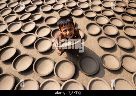 17. Mai 2022, Brahmanbaria, Chittagong, Bangladesch: Ein Kind sitzt in tausenden Tontöpfen, bevor es auf einen Markt in Brahmanbaria, Bangladesch, transportiert wird. Die Tontöpfe werden zum Trocknen unter dem brennenden Sonnenschein ausgelegt, bevor sie als Töpferei in Brennöfen geladen werden. Hier werden täglich rund 3.000 Tontöpfe hergestellt und jeder von ihnen wird für 2 Dollar (2 Dollar) verkauft. Die Töpferei, ein uralter Handel, wird nur von den Menschen der 'Pal'-Gemeinschaft (Potters Community) des Hinduismus betrieben. Seit Jahrhunderten leben sie von ihren Töpferkünsten. Auch heute noch sind ihre Töpfe Stockfoto