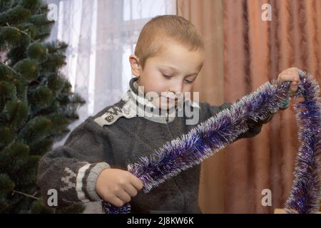 Überrascht Junge hält Lametta, um einen Weihnachtsbaum zu schmücken Stockfoto