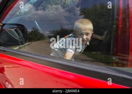 Ein Junge in einem roten Auto geschlossen und versucht, durch die Türen Auto zu bekommen Stockfoto