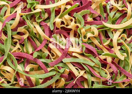 Oben mit ungekochter Fettuccine-Pasta, Hintergrund-Vollformat. Italienische dreifarbige Pasta aus Spinat, roten Rüben und weißem Pfeffer. Stockfoto