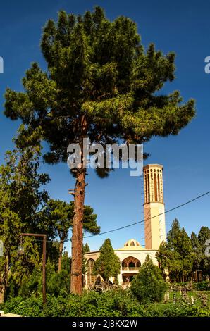 Yazd, Mehriz, Iran, 19. Februar 2021:Blick auf den Sommerpalast Dovlat Abad und den höchsten Windturm im Garten unter den alten Kiefern, Obstbäumen Stockfoto