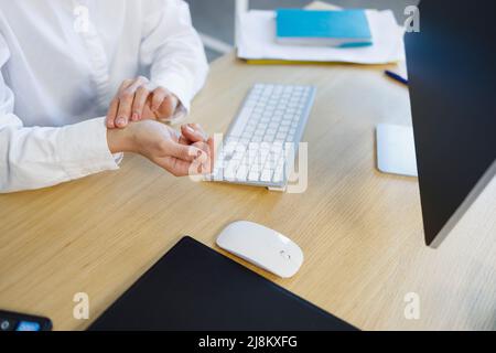 Eine Geschäftsfrau misst ihren Herzschlag, während sie am Arbeitsplatz im Büro sitzt Stockfoto