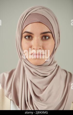 Vertikales Kopf- und Schulterporträt einer schönen jungen Frau, die einen blassrosa Hijab trägt und die Kamera anschaut Stockfoto