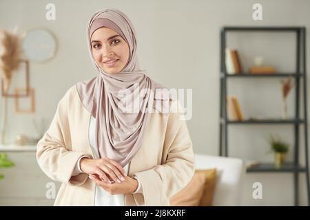 Horizontales mittleres Porträt einer jungen Frau in einem lässigen Outfit mit einem rosa Kopftuch, das vor der Kamera lächelt Stockfoto