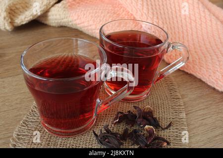 Hibiscus (Chinarose) oder heißer roter Tee im Glas auf dem Küchentisch. Stockfoto