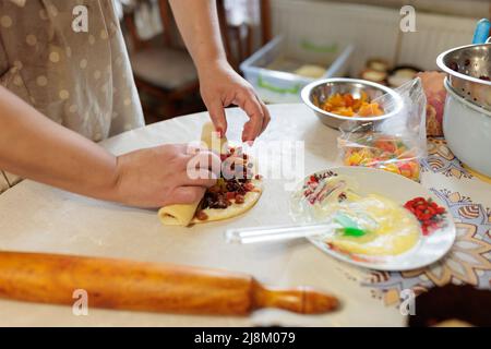 Weibliche Hände verdrehen den Teig mit Rosinen und kandierten Früchten. Roher Kuchenteig. Hausgemachte Küche Stockfoto