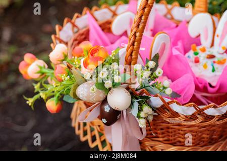Korbkorb mit hell bemalten Ostereiern und Osterkuchen mit Frühlingsblumen Stockfoto