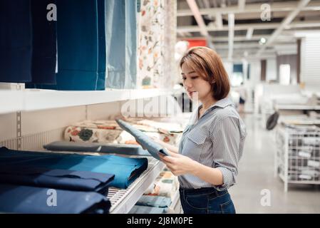 Eine asiatische Frau wählt im Einkaufszentrum Stoff und Textilien aus. Stockfoto