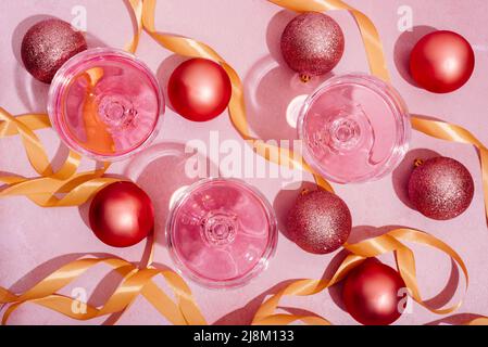 Rosafarbener Champagner in luxuriösen Kristallgläsern und weihnachtskugeln mit goldenem Bändchendekor. Draufsicht. Silvesterfeier und Nachtclub-Party mit g Stockfoto