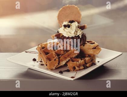 Belgische Waffeln mit Eis und Schokolade auf weißem Teller auf dem Tisch in einem Café Stockfoto