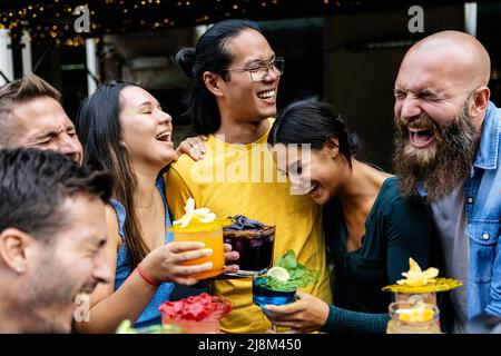 Glückliche Freunde aus verschiedenen Rassen lachen zusammen und trinken Cocktails auf der Barterrasse Stockfoto