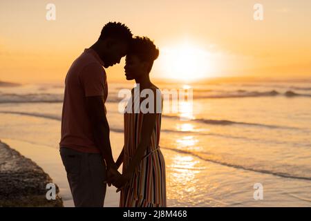 Seitenansicht eines romantischen, afroamerikanischen jungen Paares mit Kopf auf Kopf, das gegen Meer und Himmel steht Stockfoto