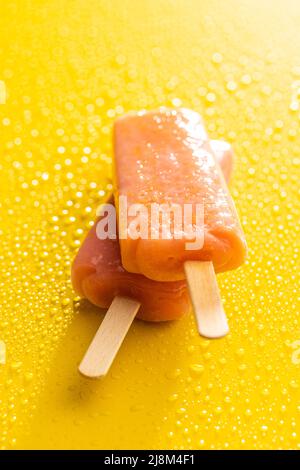 Fruchtiges Eis lolly. Süßes Fruchteis auf gelbem Tisch mit Wassertropfen. Stockfoto