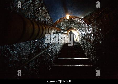 Die Silhouette eines Besuchers, der auf der Treppe spaziert, führt zum Eingang des alten Kohlebergbautunnels in Sawahlunto, einer ehemaligen Kohlebergbaustadt, die Ende des 19. Jahrhunderts von niederländischen Kolonialisten in West Sumatra, Indonesien, gegründet wurde. Stockfoto