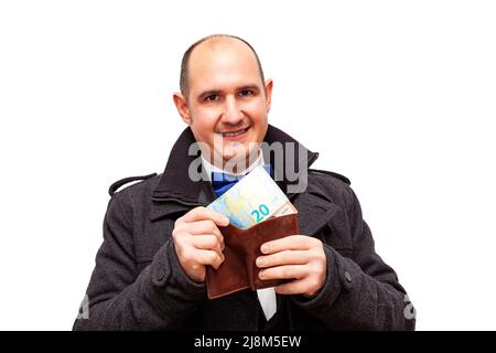 Ein kahler kaukasischer erwachsener Mann, der gut in Anzug, Hemd, Fliege und Jacke gekleidet ist, hält eine braune Lederbörse, aus der er 10 und 20 herausnimmt Stockfoto