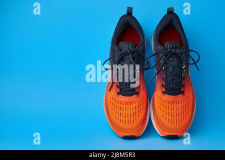 Orangefarbene Sneakers auf blauem Hintergrund mit Kopierfläche. Schuhe zum Joggen, Laufen, Fitness, körperliches Training Stockfoto