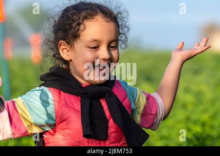 Selektive Fokusaufnahme eines glücklichen Mädchens in pinkem Outfit mit schwarzer Weste über der Schulter und offenen Händen. Stockfoto