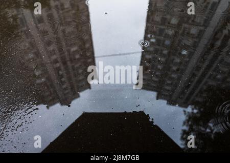 Spiegelung von Gebäuden und ein Regenschirm in einer Pfütze auf dem Asphalt nach dem Regen. Abstrakte Fotografie. Stockfoto