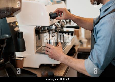 Nahaufnahme von Barista-Händen, die Milch im Krug mit Dampf aufheizen Stockfoto