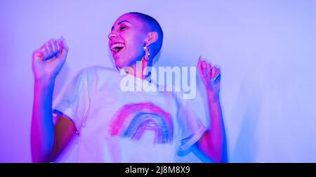 Unbeschwerte junge Frau tanzt freudig, während sie allein im hellen Neonlicht steht. Fröhliche junge Frau, die Spaß hat und sich an einem Hous amüsieren Stockfoto