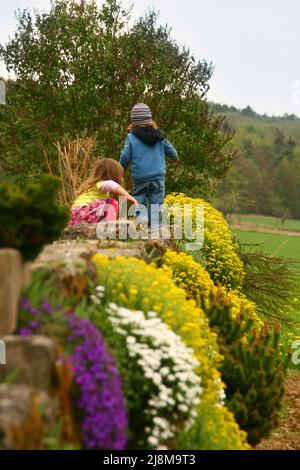 Deutschland, Bayern, Unterfranken, Leinach. 29 vom April 2012. Kleine Jungen und Mädchen klettern die Steineinfassung mitten im Alpengarten Stockfoto