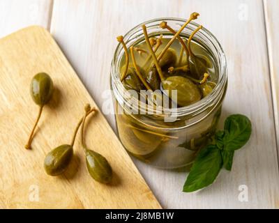 Marinierte Kaperfrüchte in einem offenen Glas auf einem Holztisch. Picled Kaper Beeren zum Würzen und Garnieren. Caperberry aus der Dose. Mediterrane Küche Stockfoto