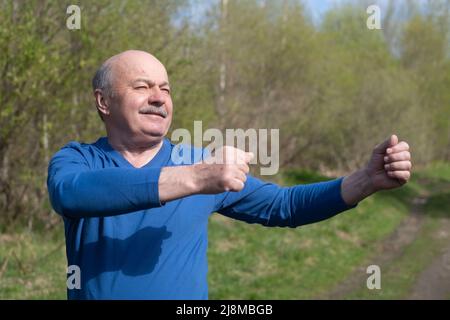 Seniorläufer mit Armreif beim Stretching. Frühling Natur. Gesunde Lebensweise im Alter. Stockfoto