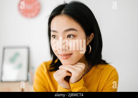 Nachdenkliche und nachdenkliche asiatische Frau schaut weg zu Hause bleiben Stockfoto