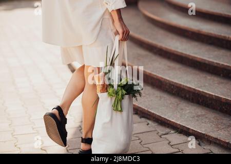 Rückansicht einer unverkennbaren stilvollen Frau, die beim Spaziergang auf der Straße eine Öko-Einkaufstasche mit Lebensmittelwaren im Freien hält Stockfoto