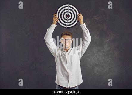 Porträt eines selbstbewussten Mannes, der auf grauem Hintergrund Darts über den Kopf hält. Stockfoto