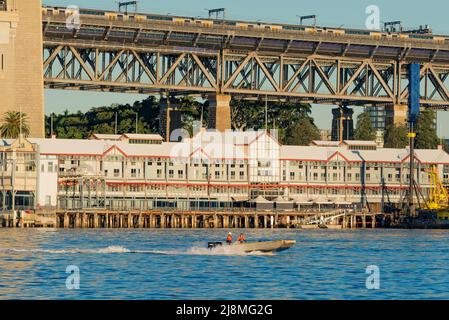 Zwei Männer in hoch sichtbarer Kleidung und Schwimmwesten bewegen sich auf einem kleinen Handelsschiff mit zwei Außenbordmotoren mit hoher Geschwindigkeit durch den Hafen von Sydney in Australien Stockfoto