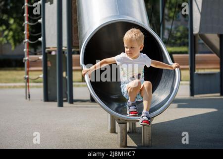 Fröhliches Kind, das in der Schlauchrutsche auf dem Kinderspielplatz spielt. Stockfoto