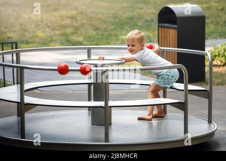 Der kleine Junge spielt auf dem Spielplatz im Park. Kind dreht ein Karussell. Stockfoto