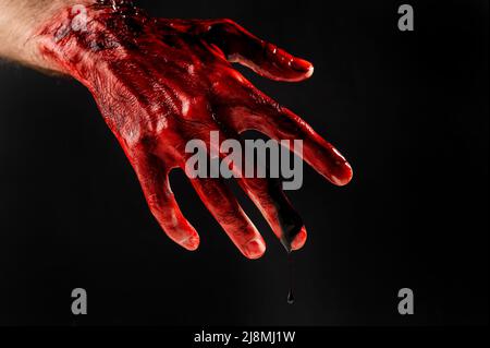 Nahaufnahme einer mit Blut befleckten männlichen Hand auf schwarzem Hintergrund. Stockfoto