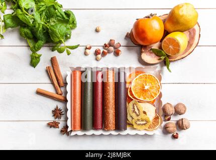 Obstpastilien verschiedener Geschmacksrichtungen und Fruchtchips oder Trockenobstscheiben in einer Geschenkbox, umgeben von frischen Früchten, Nüssen und Gewürzen und frischem Basilikum Stockfoto