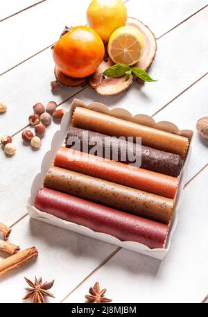 Obstpastilien verschiedener Geschmacksrichtungen in einer Geschenkbox, umgeben von frischen Früchten, Nüssen und Gewürzen sowie frischen Basilikumblättern Stockfoto