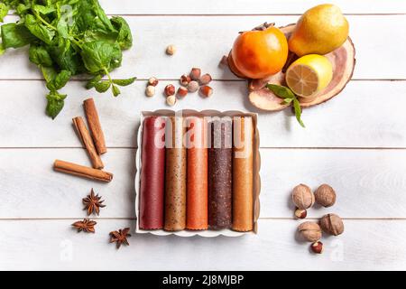 Obstpastilien verschiedener Geschmacksrichtungen in einer Geschenkbox, umgeben von frischen Früchten, Nüssen und Gewürzen sowie frischen Basilikumblättern Stockfoto