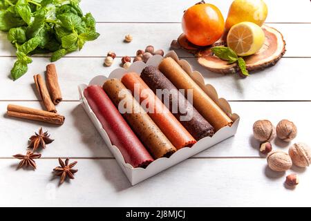 Obstpastilien verschiedener Geschmacksrichtungen in einer Geschenkbox, umgeben von frischen Früchten, Nüssen und Gewürzen sowie frischen Basilikumblättern Stockfoto