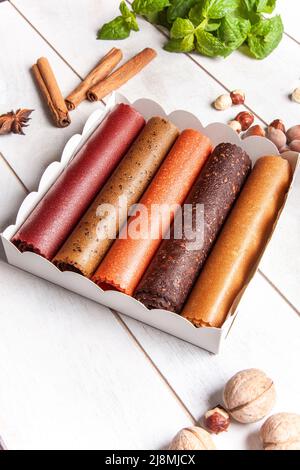 Obstpastilien verschiedener Geschmacksrichtungen in einer Geschenkbox, umgeben von frischen Früchten, Nüssen und Gewürzen sowie frischen Basilikumblättern Stockfoto