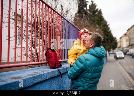 Vater bringt seine kleine Tochter mit Down-Syndrom zur Schule, draußen auf der Straße. Stockfoto