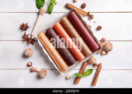 Obstpastilien verschiedener Geschmacksrichtungen in einer Geschenkbox, umgeben von frischen Früchten, Nüssen und Gewürzen sowie frischen Basilikumblättern Stockfoto